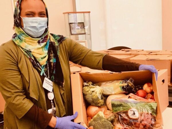 A Charles River Community Health staff member displays an open Speedway Produce box filled with fresh fruits and vegetables. The Speedway Produce Program is an initiative by the Architectural Heritage Foundation (AHF) to combat food insecurity in Brighton during the COVID-19 pandemic.