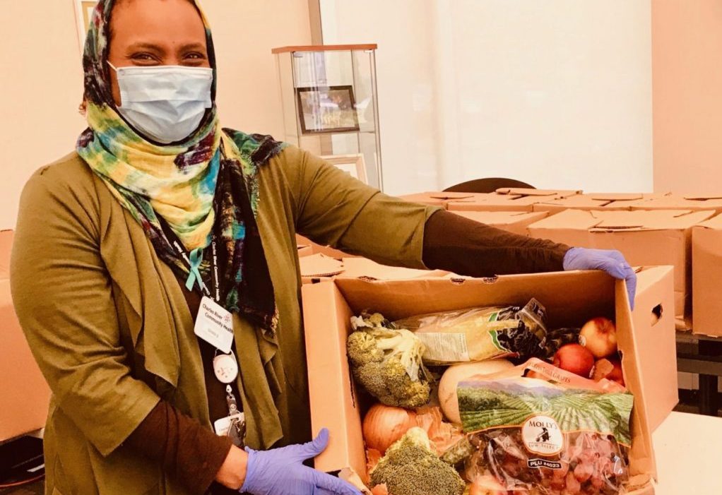 A Charles River Community Health staff member displays an open Speedway Produce box filled with fresh fruits and vegetables. The Speedway Produce Program is an initiative by the Architectural Heritage Foundation (AHF) to combat food insecurity in Brighton during the COVID-19 pandemic.